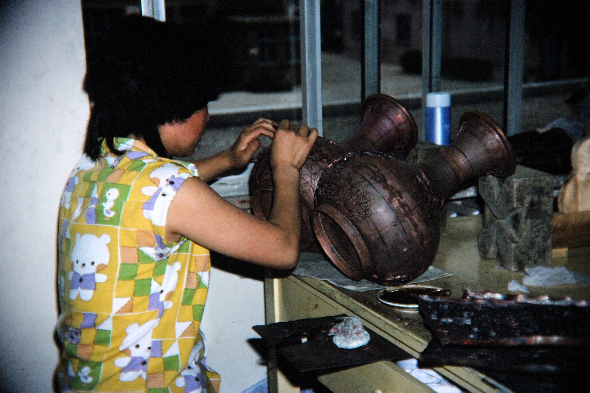 A craftswoman at Beijing's cloisonné workshop solders fine copper wires onto the rims of two large vases — the first stage of jingtailan enamel work