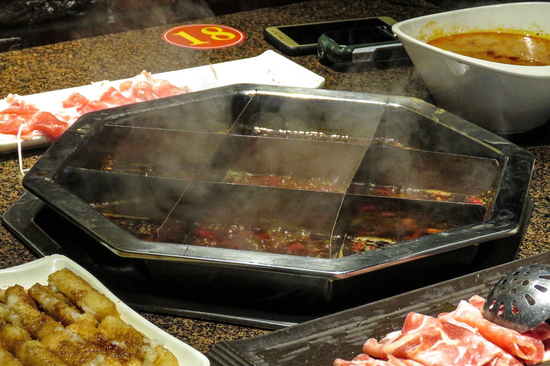 A nine-grid Chongqing hotpot with red tallow broth, surrounded by plates of tripe, sliced meat and vegetables