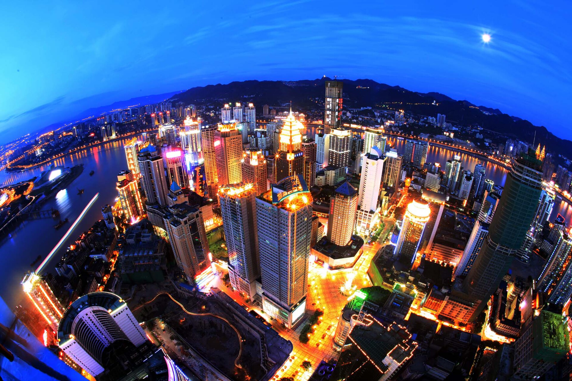 The Yuzhong peninsula at blue hour from above — towers lit in gold and blue, the Jialing and Yangtze rivers curving around the old centre of Chongqing