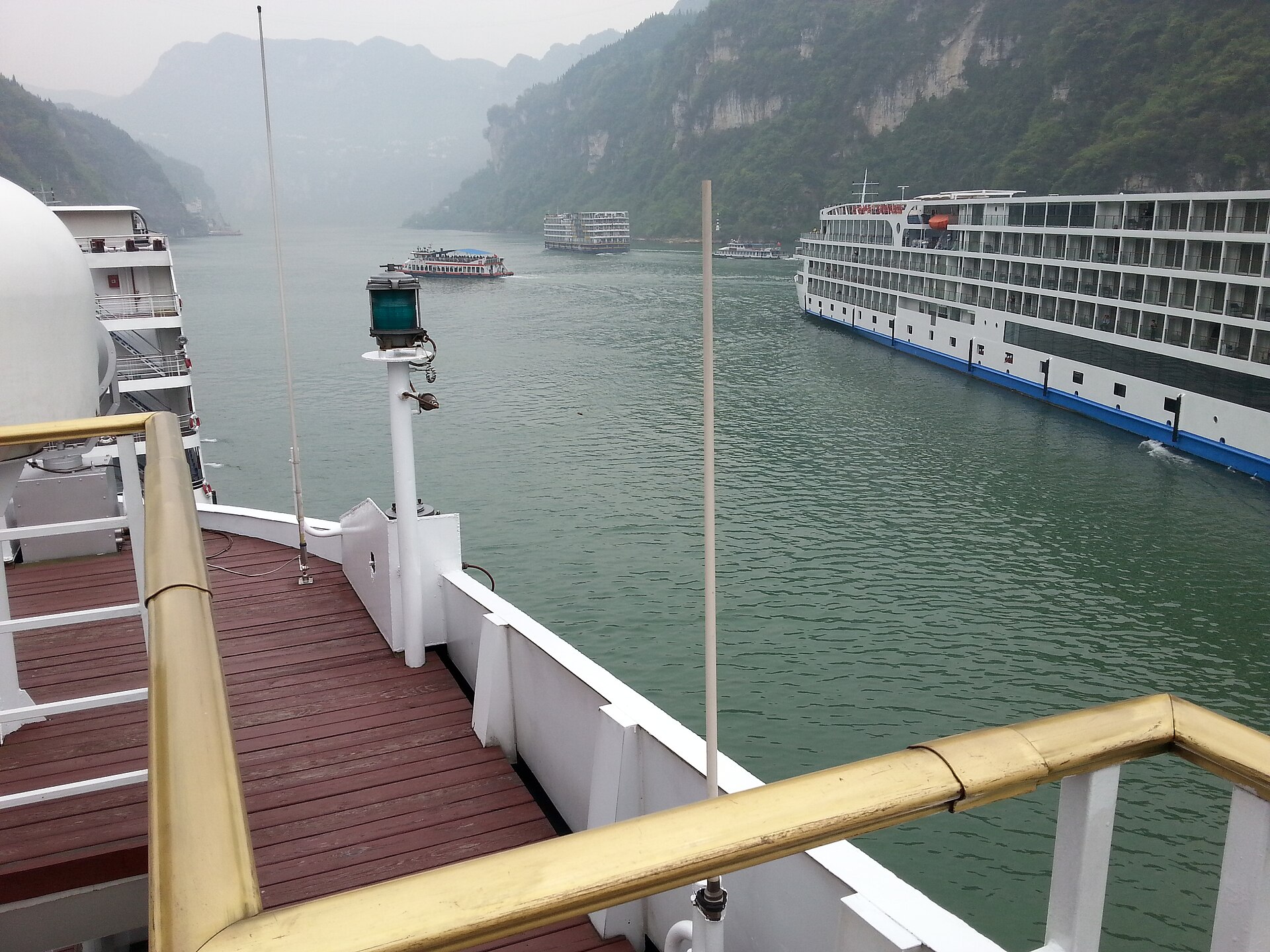 Cruise ships passing each other on the Yangtze River between the green walls of the Three Gorges, seen from an open deck