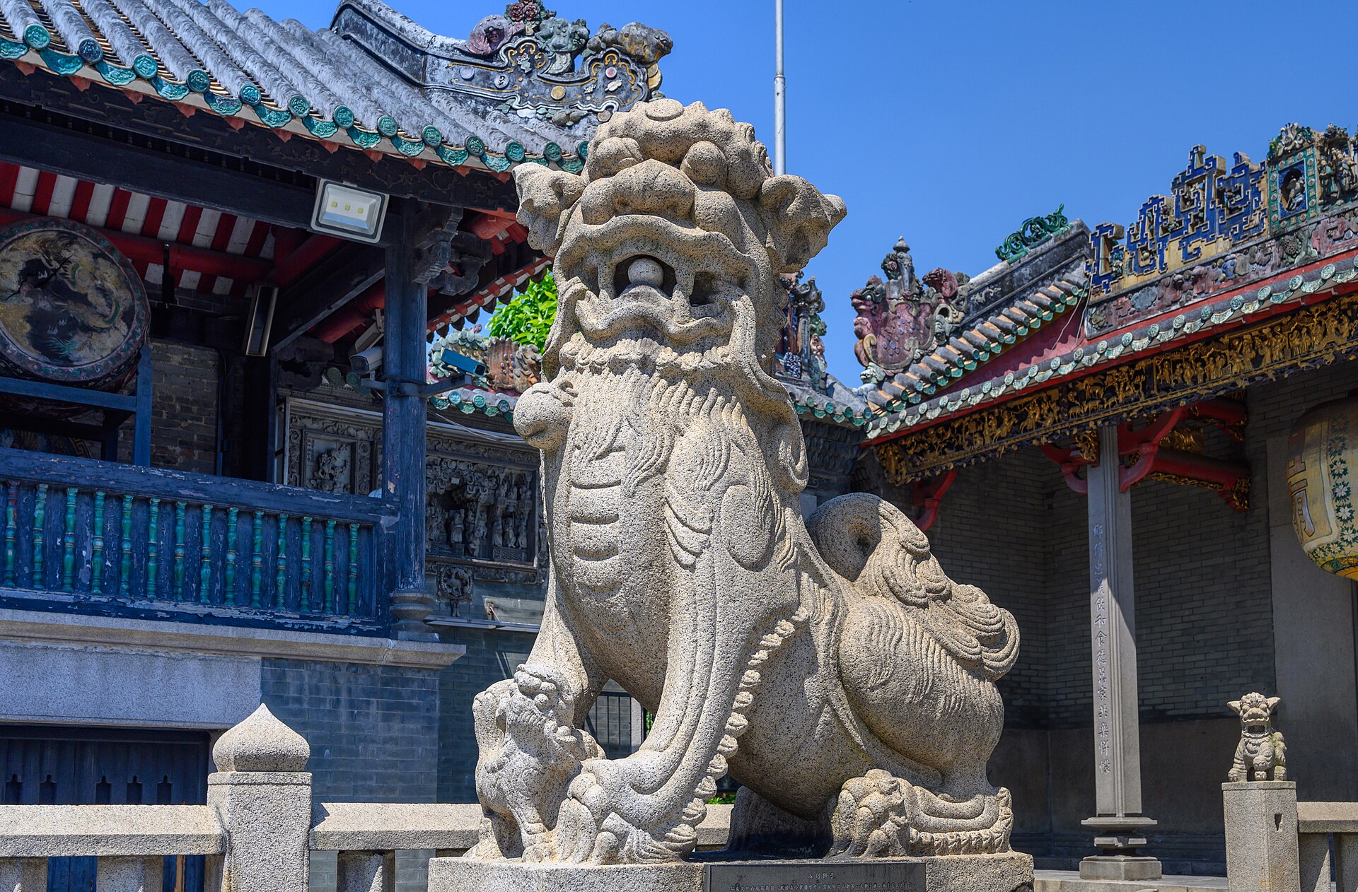A carved stone lion in front of the performance stage at the Foshan Ancestral Temple, with Shiwan ceramic roof ridges behind