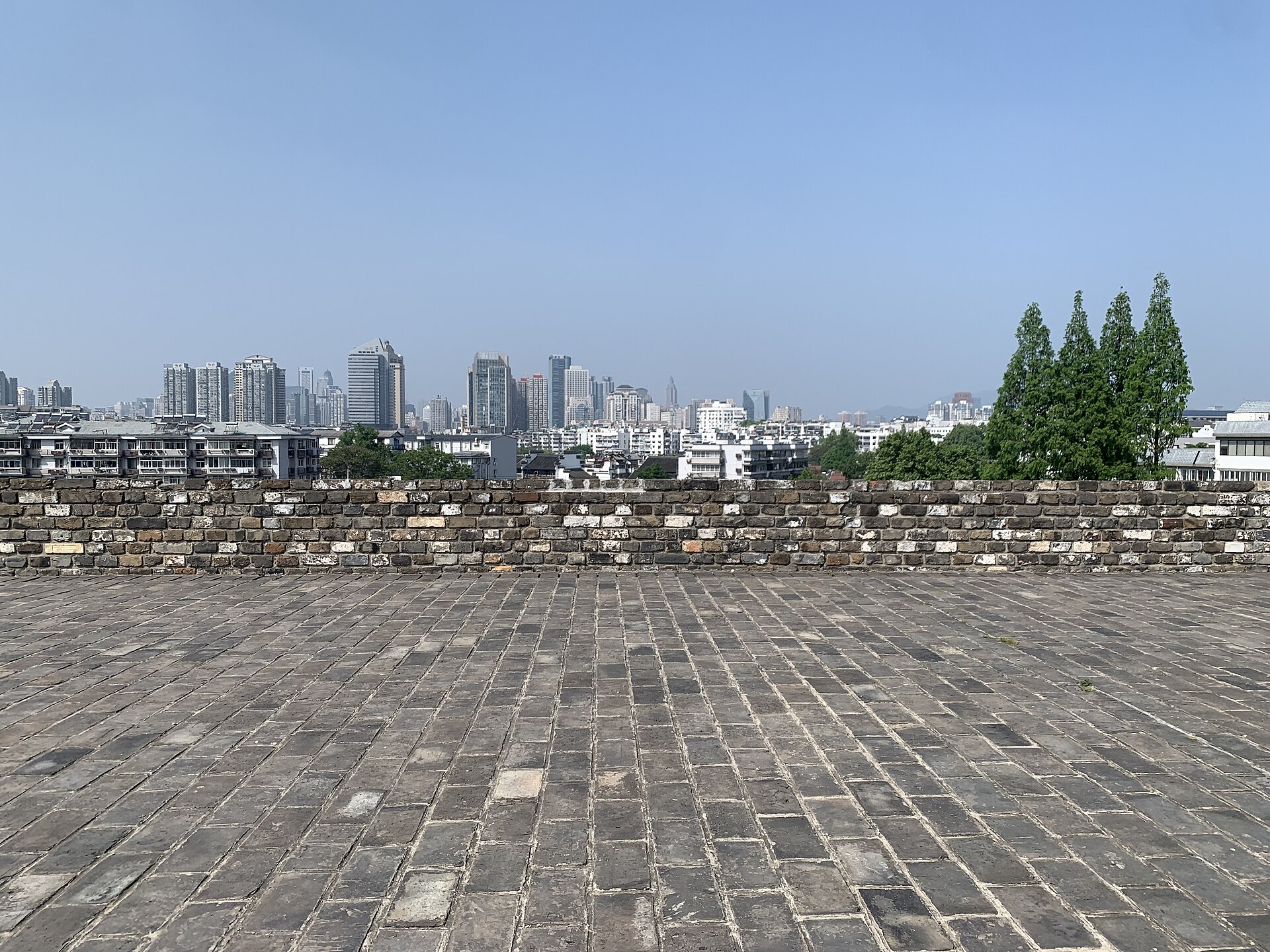 The broad brick top of Nanjing's Ming city wall, its inscribed parapet bricks facing the modern skyline