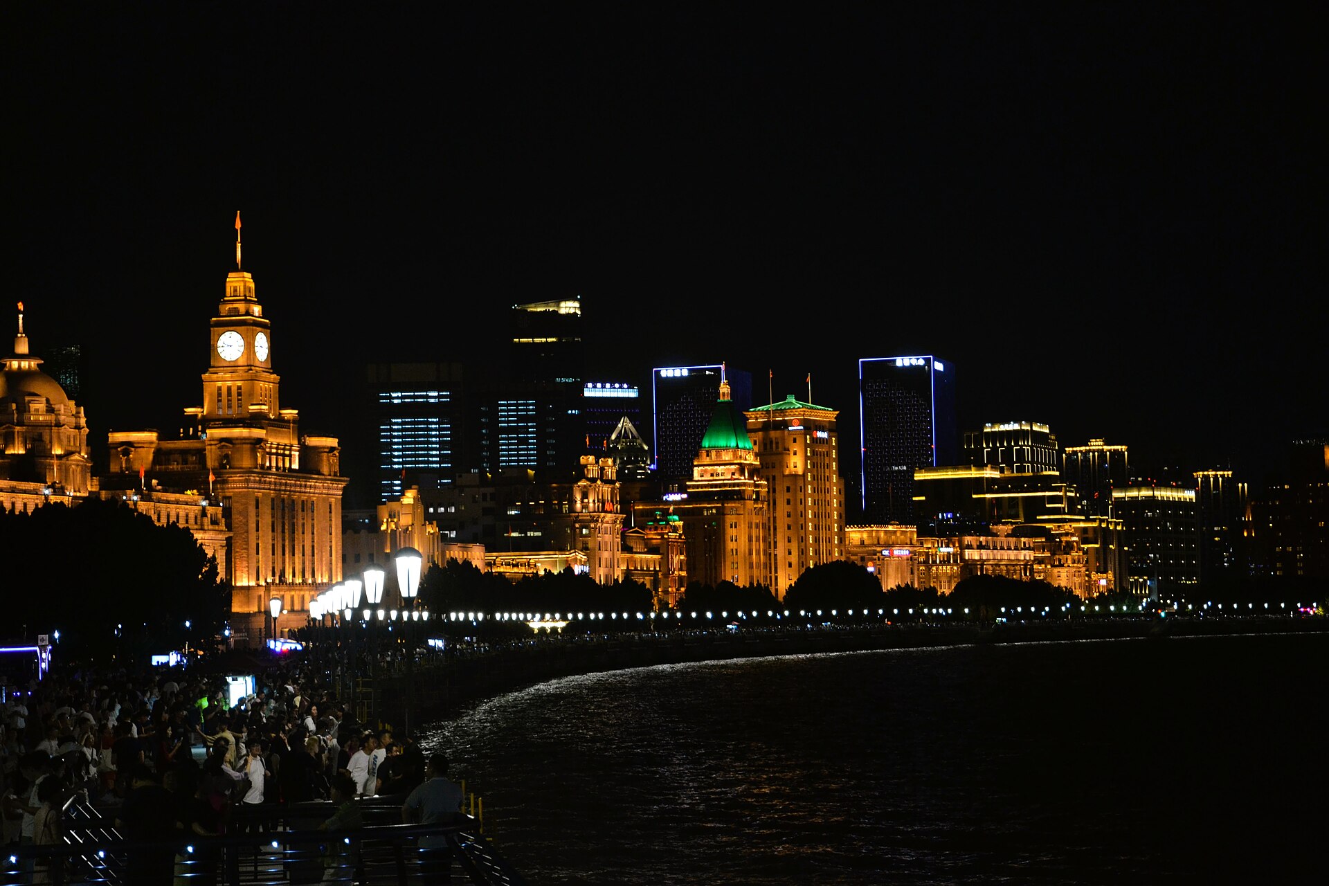 The Bund waterfront and its clock tower lit after dark, photographed from across the Huangpu River
