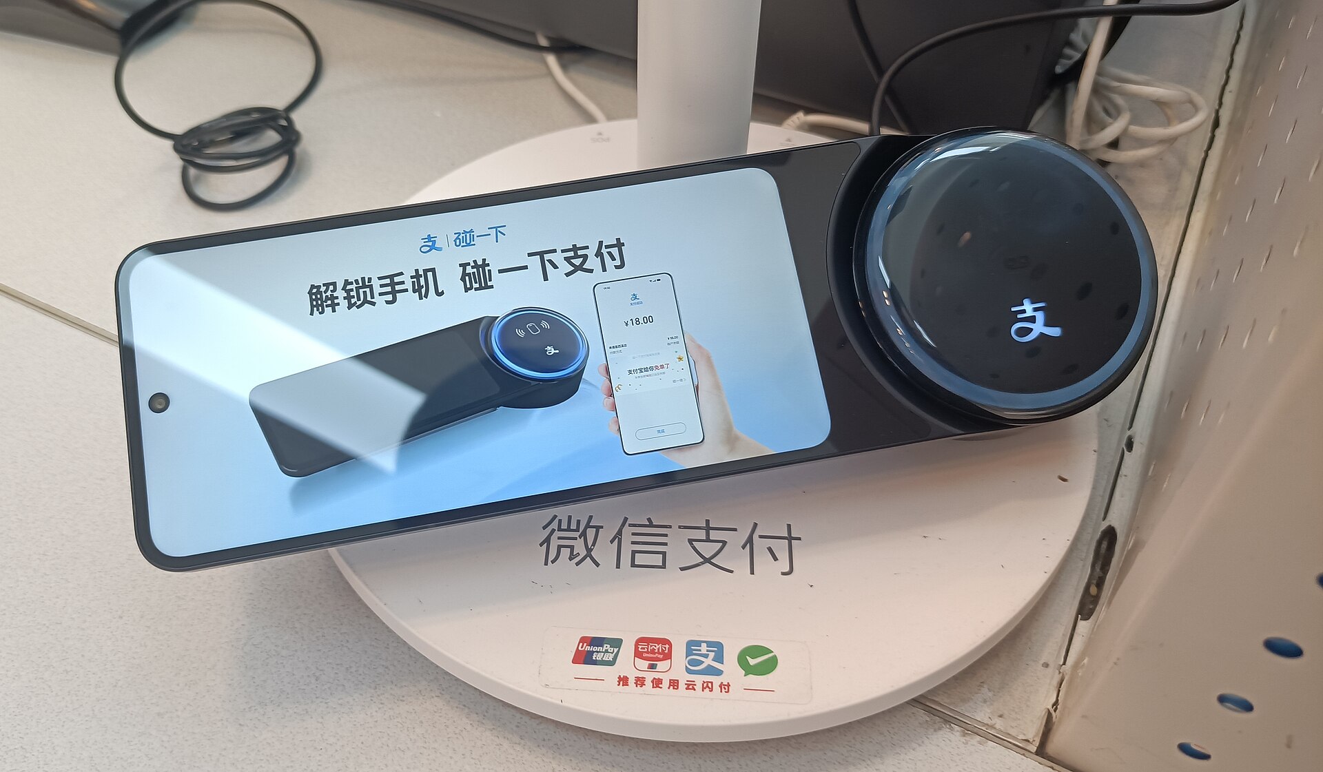 A tap-to-pay payment terminal on a shop counter in China, showing Alipay and WeChat Pay acceptance marks