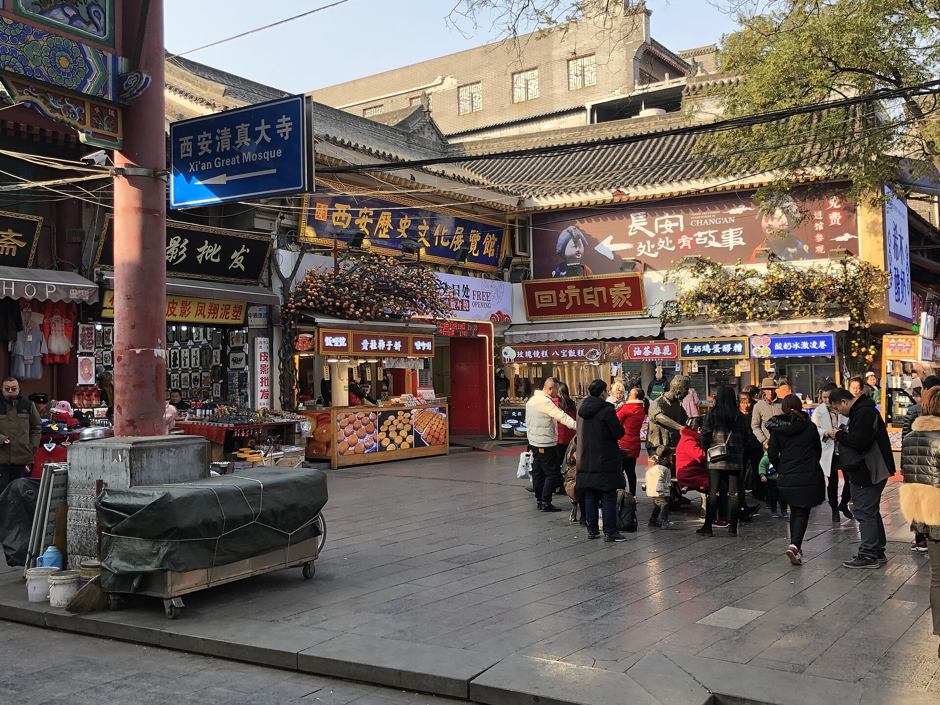 Daytime shoppers at food and craft stalls in Xi'an's Muslim Quarter, with a shadow-puppet shop on the left